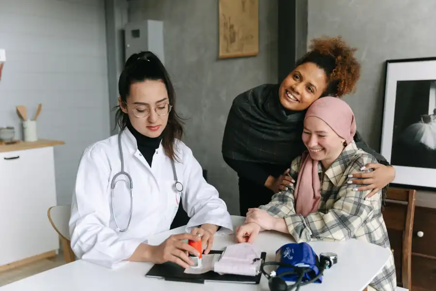 Médica conversa com uma paciente de lenço, que é abraçada por uma amiga