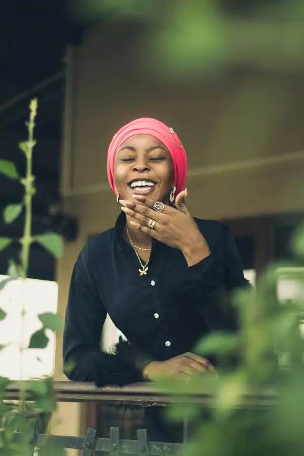 Mulher de lenço rosa sorrindo com a mão no rosto